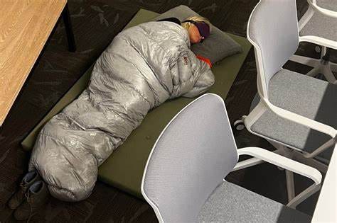 image of a woman sleeping in a sleeping bag on a conference room floor